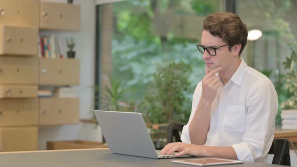 Young Man Thinking While Working on Laptop in Modern Office