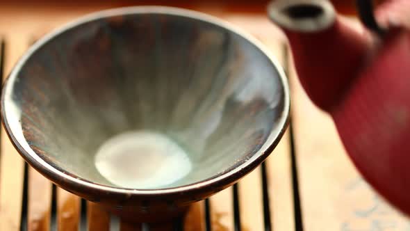 Tea is Poured Into a Bowl From a Red Chinese Teapot