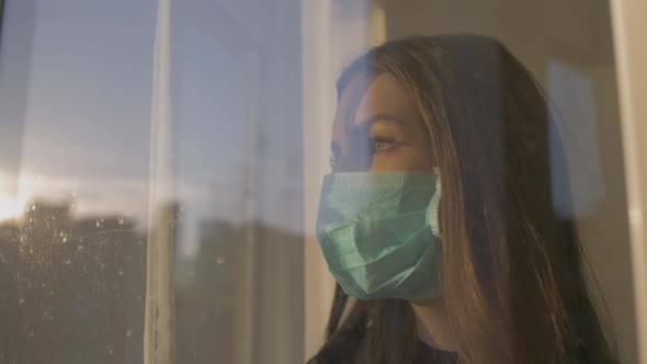 A Woman in a Protective Mask Looks Out the Window