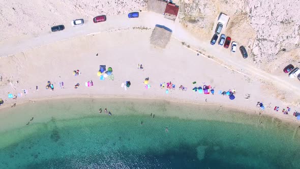 Flying above parked cars and people on sandy beach of Pag island