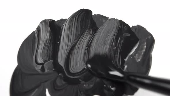Paintbrush draws black paint on a white canvas with bold strokes