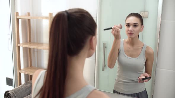 Face Makeup. Woman Using Powder And Looking In Mirror