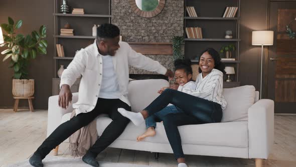 African Family Parents and Little Daughter Child Girl Jumping Falling on Comfortable Soft Sofa