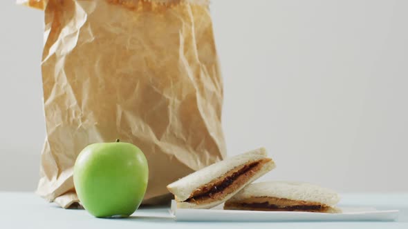 Peanut butter and jelly sandwich with apple and paper bag against white background