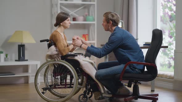 Side View Confident Loving Man Supporting Depressed Sad Woman in Wheelchair