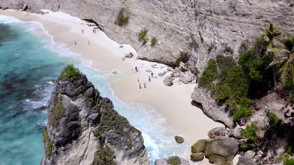 People bathing on Diamond Beach in Nusa Penida island Indonesia behind rock spire structure, Aerial