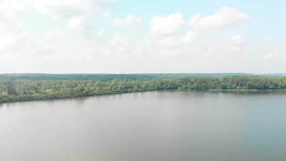 forward drone flight to a forest tree line and horizon of blue sky and white clouds on a summer day