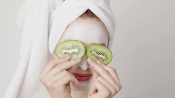 Close Up of a Girl with White Mask on Her Face and a Towel on Her Head Closing Her Eyes with Kiwi