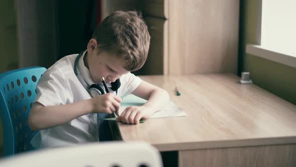 Schoolboy Does Homework Sits in Headphones Draws in a Notebook with a Triangular Yardstick