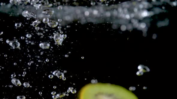 Closeup of fresh kiwis slices falling into clear water with big splash on black background. 