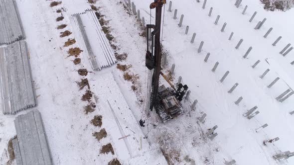 Aerial drone view of a pile bore machine and worker at winter construction site 22