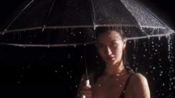 Young Woman in Black Swimming Suit Standing Under the Rain and Holding an Umbrella Water Drops