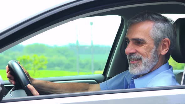 Senior Man Sits in the Car and Rajoices - Closeup Shot From Side - Countryside in the Background