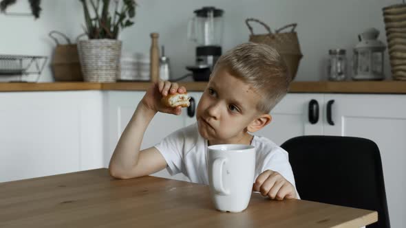 Close-Up of A Child Boy Having Lunch, Eating A Pie and Drinking Tea, Is in the Kitchen
