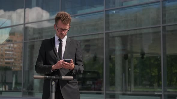 Man Is Typing Message at Smartphone on Street in Business District