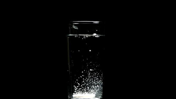 Dissolving Pill Falls Into Glass of Water Dissolves Isolated on Black Backdrop