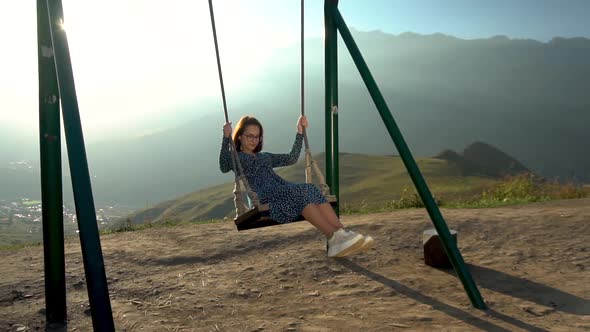 Young Woman Goes for a Drive on a Swing Against a Background of Mountains. The Sun Shines Brightly