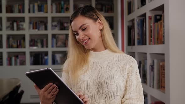 Portrait of a Young Female Student in the Library with a Tablet