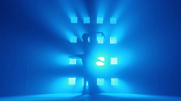 Graceful Silhouette Ballerina Doing a Workout in the Classroom. Smoke in the Rays of Blue Light