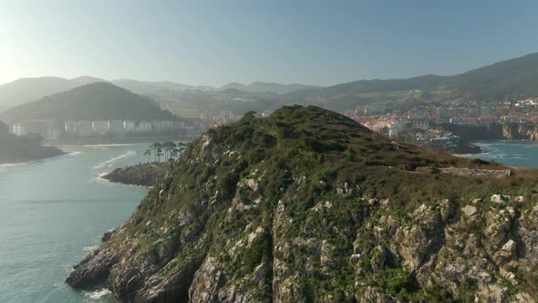 Flyover greenery San Nicolas island revealing Lekeitio scenic Bay and Cityscape, Spain