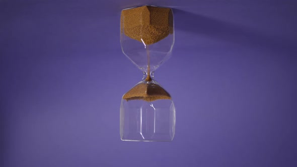 Glass Hourglass with Golden Sand on Purple Background