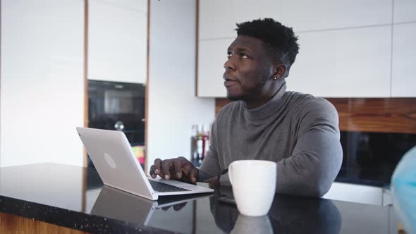 Young Black Man Using Laptop in His Appartment. Remote Work Concept