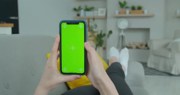 Woman at Home Lying on a Couch Using Smartphone with Green Mock-up Screen, Doing Swiping, Scrolling