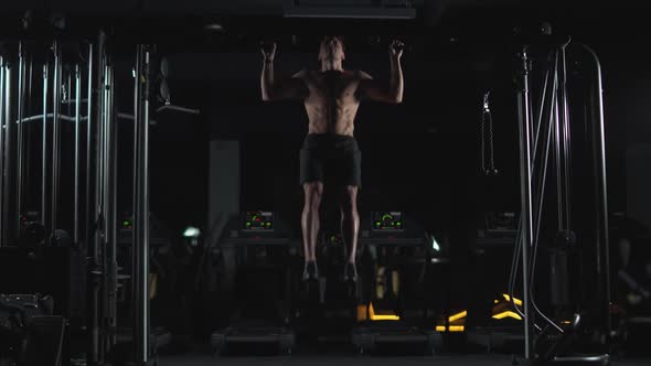 Wellness Athletic Man Performs Pullups on the Horizontal Bar Strength Training in the Gym at Night