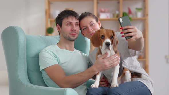 Young Couple with Dog Taking Selfie Photo and Sitting on Sofa in Home Room Spbi