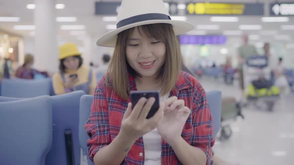 Asian woman using smartphone while sitting on chair waiting her flight in international airport