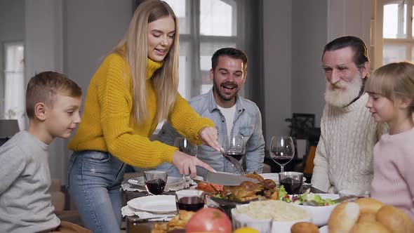 Smiling Woman in Knitted Sweater Carving Roast Turkey During Family Festive Dinner