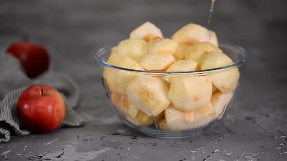 Woman pouring lemon juice over apple slices in glass bowl.