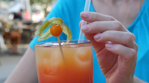 A Woman Holds a Cocktail Tube in Her Fingers