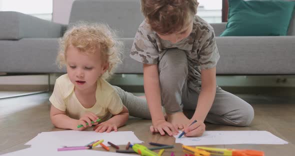 A Little Boy and a Little Girl are Drawing with Pencils on the White Paper on the Floor