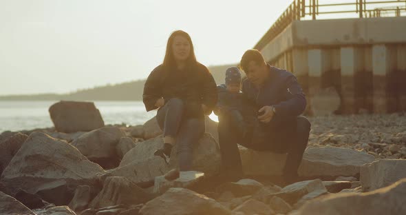 International Family Sits on the Pier on Large Rocks