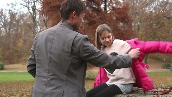 Father helping daughter put on jacket in the park