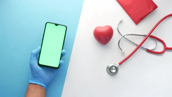 Doctor Hand Holding Smart Phone with Blank Screen on Clinic Desk