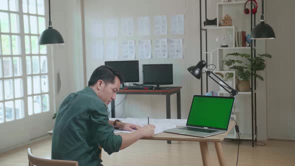 Asian Man Drawing Storyboard Animation Comic Cartoon With Mock Up Green Screen Laptop Computer