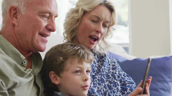 Happy caucasian grandparents with grandson using tablet and sitting in living room