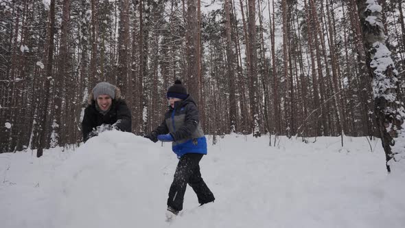 Caucasian Family with Smile Quickly Roll Large Snow Ball in Forest