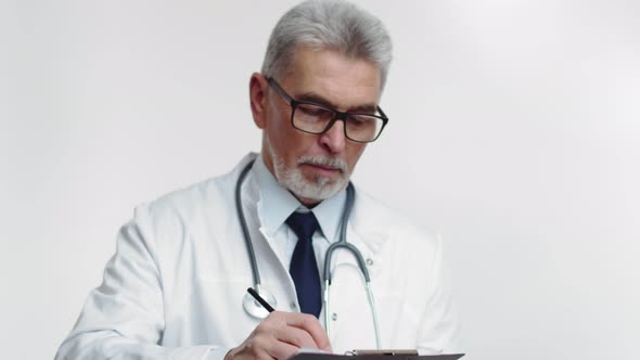 Attending Physician in Glasses and Medical Coat Makes Notes in Tablet Looks Up and Writes Something