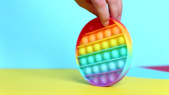 female hand plays with a children silicone pop it toy on a multicolored background