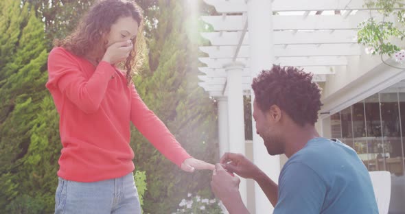 Happy biracial man proposing on knees with ring to surprised woman