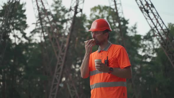 Engineer Having Lunch Near Power Lines and Electricity Pylons in the Field