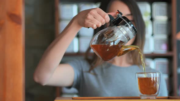 Young Smiling Woman Pouring Red Tea From Glass Kettle to Smal Cup