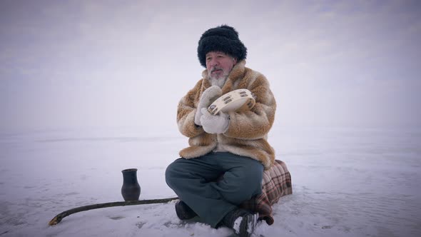 Concentrated Shaman Drumming Tambourine Sitting on Frozen Arctic Ocean