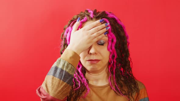 Young Woman Looking at Camera and Doing Facepalm on Red Background