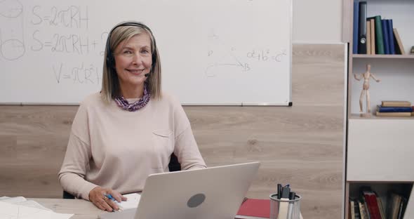 Portrait of Positive Senior Woman in Wireless Headset with Microphone Looking To Camera