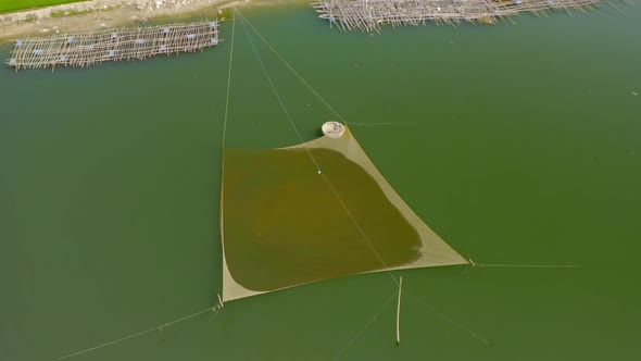 Drone view of a fisherman is preparing fishing trap on the river for catching fish. He's driving a b