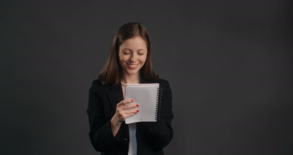 Young Woman in Black Suit Smiles and Writes Her Ideas to the Paper Notepad Making the Notes with